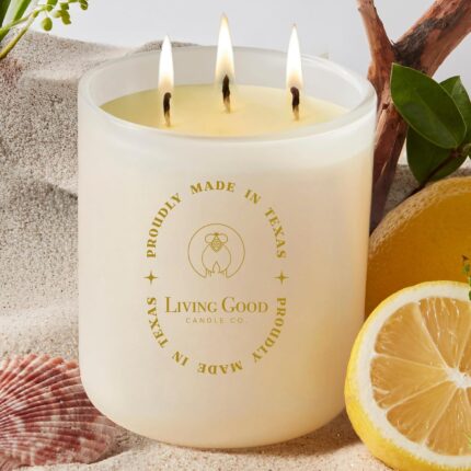 A warm yellow beeswax candle in a clear glass jar with three wicks, set against a light background.