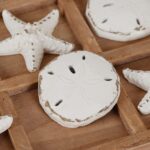 A distressed white NIKKY HOME Beach Tic Tac Toe game board with starfish and sand dollar resin pieces.