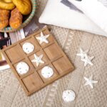 A distressed white NIKKY HOME Beach Tic Tac Toe game board with starfish and sand dollar resin pieces.