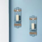 Two blue wooden starfish wall candle sconces with hemp rope accents, holding small candles, mounted against a light wall.
